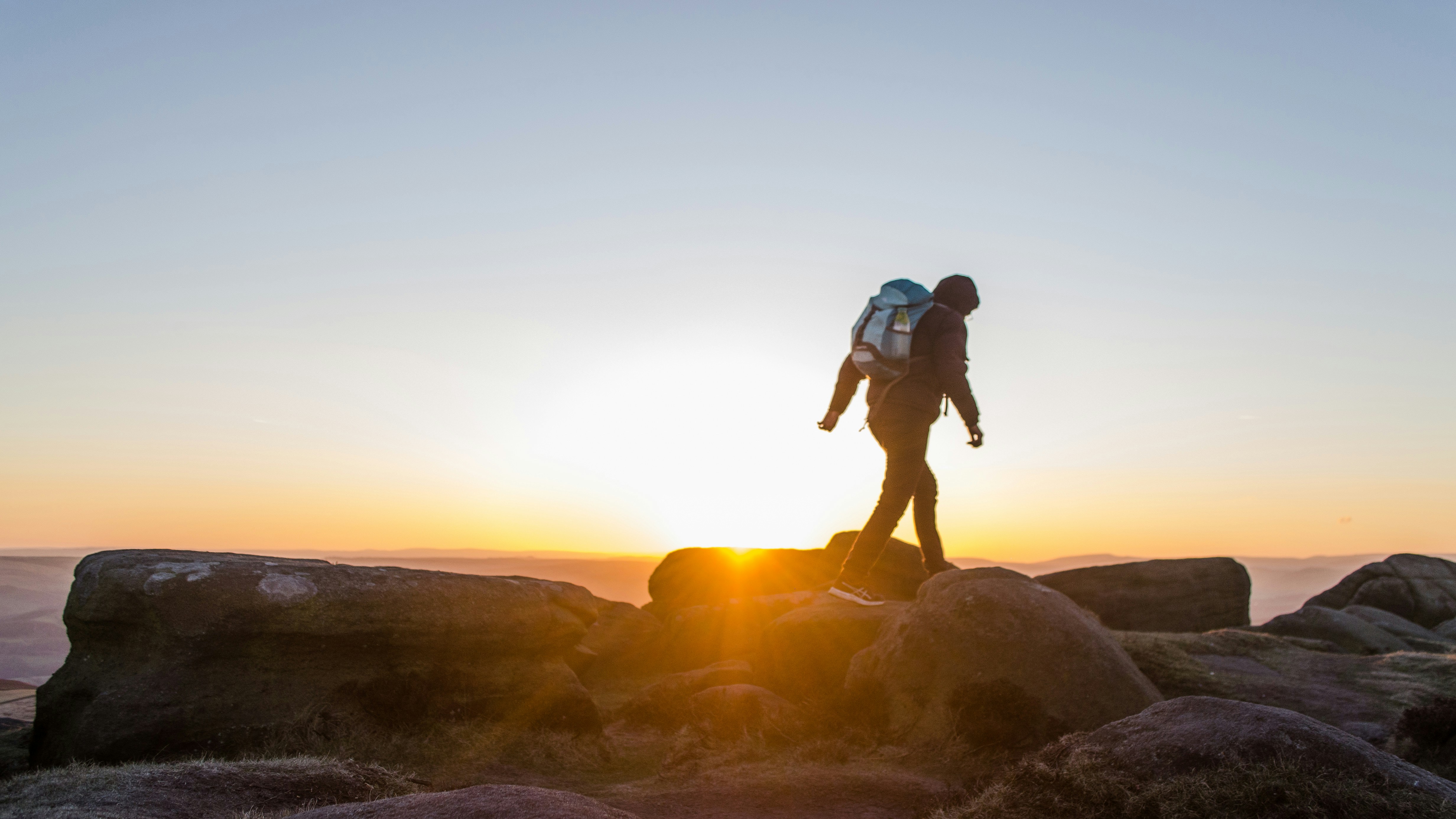 Hiker standing on the gritstone cliffs of Stanage Edge at sunset, overlooking the rolling moors and valleys of the Peak District